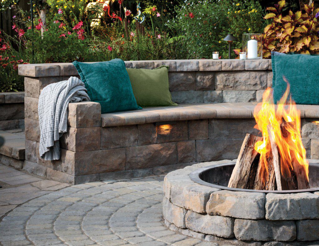 A stone bench curved around a fire pit; the bench has tidepool and seagrass colored throw pillows on it.